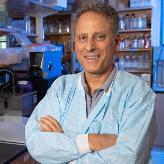 Mark Prausnitz poses with arms crossed in his lab with shelves of materials and bottles in the background.