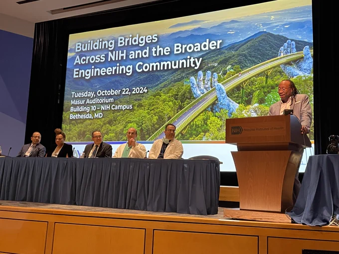 A photo of Manu Platt moderating a panel of speakers during an NIH event