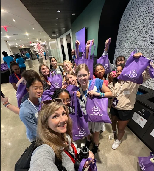 Selfie featuring a group of girls holding up purple take home bags from Amazon Web Services Girls' Tech Day.
