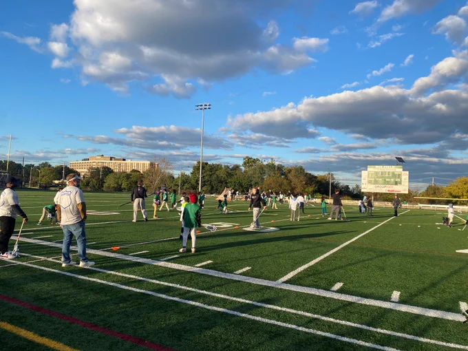 A large group of local children receive instruction from college lacrosse players and law enforcement officers. 
