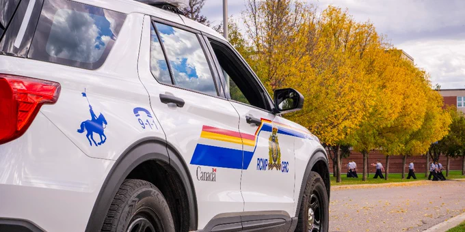 An RCMP car parked on the side of the road as cadets march in the background.