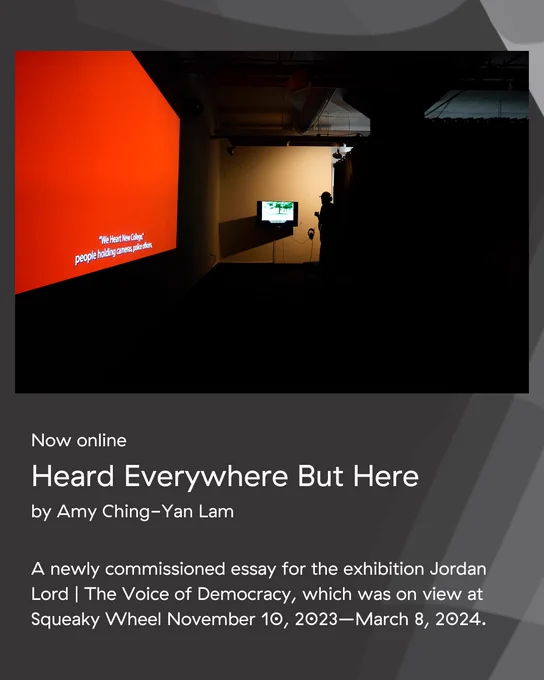 An image with text underneath. The text states: “Now online. Heard Everywhere But Here by Amy Ching-Yan Lam. A newly commissioned essay for the exhibition Jordan Lord | The Voice of Democracy, which was on view at Squeaky Wheel November 10, 2023–March 8, 2024. The image is a view of the installation of Jordan Lord’s exhibition “The Voice of Democracy” in Squeaky Wheel’s gallery space. On the left is “I Didn’t Set Out to Make a Film About Religion”, a red projected image on a wall, with a red color field and the captions “‘We Heart New College”, people holding cameras, police officers”. On the far end of the room is a person looking at a dimly lit television screen wearing headphones, featuring “An All-Around Feel Good”. On the television are a tree and captions underneath.