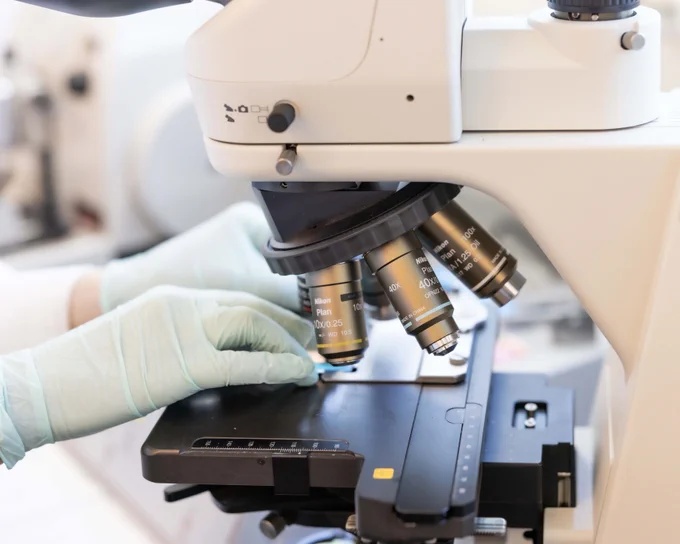 Gloved hands adjust a microscope in a research lab. 