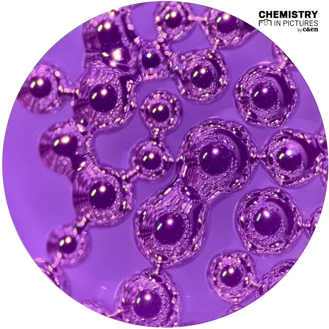 About 20 shiny droplets of liquid gallium can be seen at 40 times magnification through the scope of a dissection microscope and a purple filter.