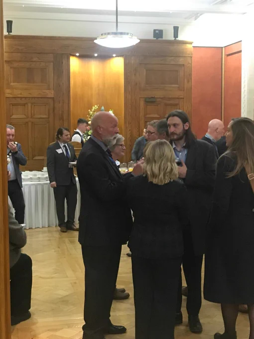 Photo of a group standing chatting, including Stephen Aston, chair of NI in a wood-panelled room in Stormont.