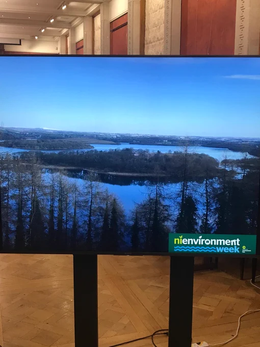 Screen showing a photo of wooded lakes under blues skies in NI, with the NI Environment Week logo