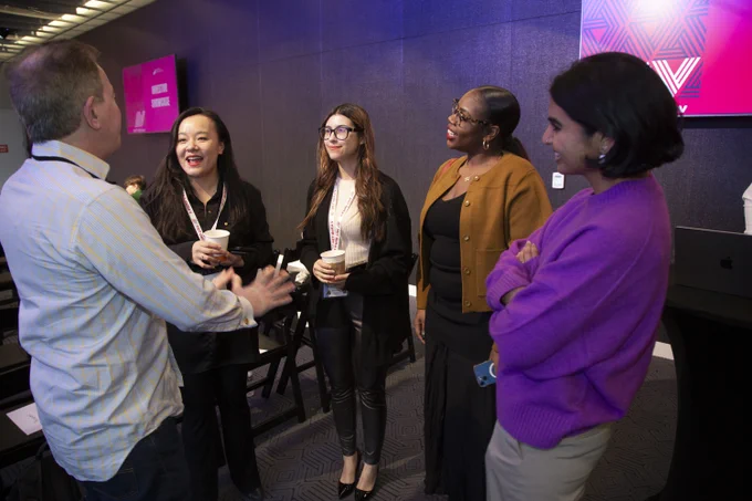 A group of young women in a high tech lecture hall interacting with an older man.