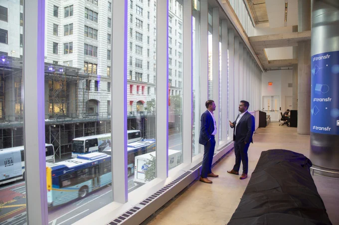Two men standing next to 30 foot windows that look out over a busy street in the Union Square neighhborhood of New York.
