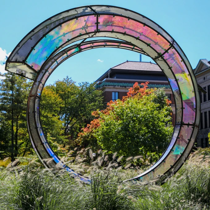 A colorful spiral sculpture at the University of Michigan with trees in the background