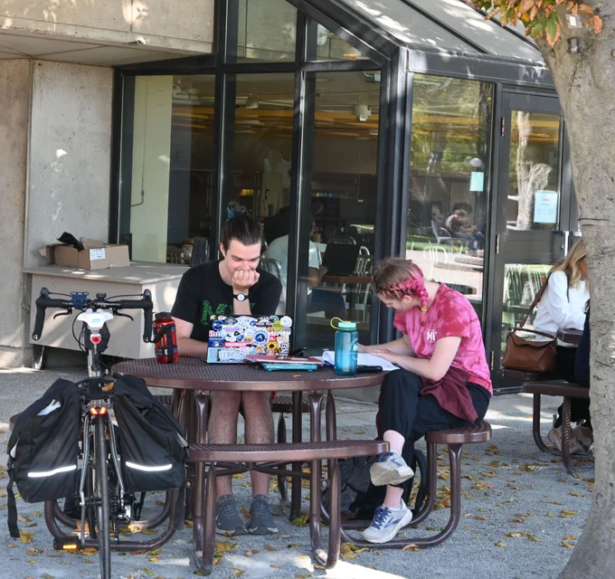 Two students sitting at a picnic table outside MIT's student center.