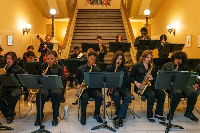 This photo shows a group of students dressed in black formal attire playing a variety of instruments. 
