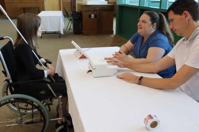 Two election workers checking a voter with a disability in to the poll site. 
