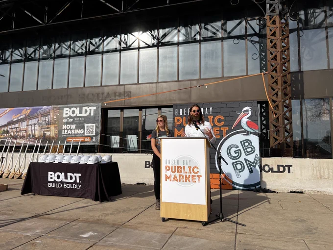 Garritt Bader, a member of the Green Bay Public Market capital campaign, speaks from a podium during the market’s groundbreaking ceremony while On Broadway’s Brooke Hafs looks on.