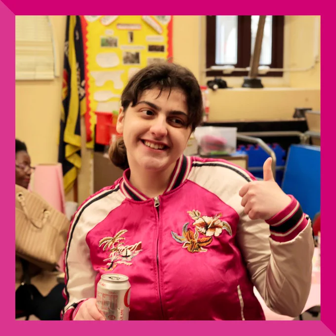 Lourdes wearing a pink jacket, giving a thumbs up