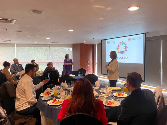 Foto de un grupo de personas participando en una discusión en torno al proyecto internacional "Solidaridad Energética en América Latina." La imagen muestra a lxs participantes sentadxs en una sala de conferencias mientras la Senadora Laura Itzel Castillo Juárez habla frente a una pantalla que proyecta el logotipo del proyecto.