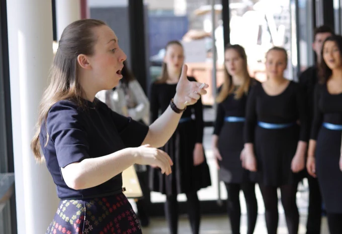 A young female conductor raises her arms to lead a group of young singers