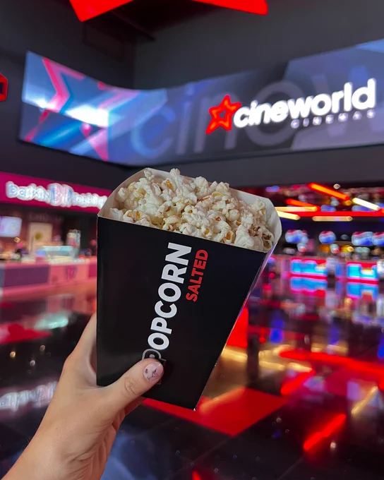 A person holding a Popcorn bucket in a vibrant cinema setting.