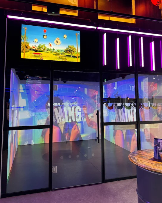 Interior view of a modern electronic gaming space featuring multiple vibrant displays, neon lights, and thematic decor.