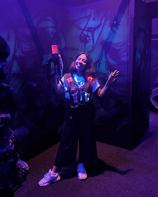 Person standing in Laserzone with eerie blue and purple lighting, surrounded by spooky trees and fog effects.