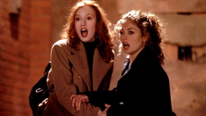 On the right, a still from the 1998 film URBAN LEGEND showing two college-aged female characters (Alicia Witt and Rebecca Gayheart) dressed for cold weather, open-mouthed and clutching each other in fear at something coming at them from off-camera.