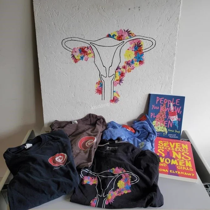 Photo of a painted flower uterus on a white background 4 shirts and 2 books in fright of it.