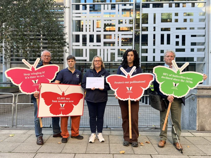 Group of Butterfly Conservation staff, trustees and a youth panel member stood outside Defra head office, holding colourful butterfly placards and an envelop addressed to Defra