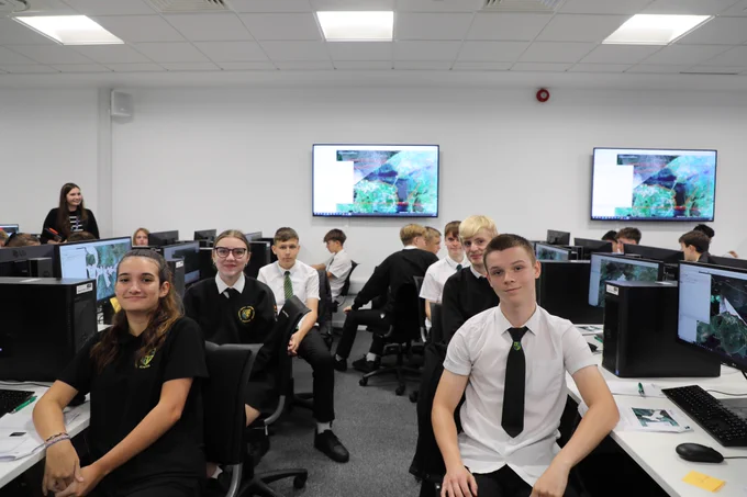 A group of students seated in front of computers in a classroom, posing for a picture. The students are dressed in uniforms.