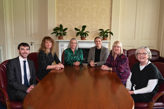 Junior Ministers Aisling Reilly and Pam Cameron sitting at a table with four Red Cross colleagues