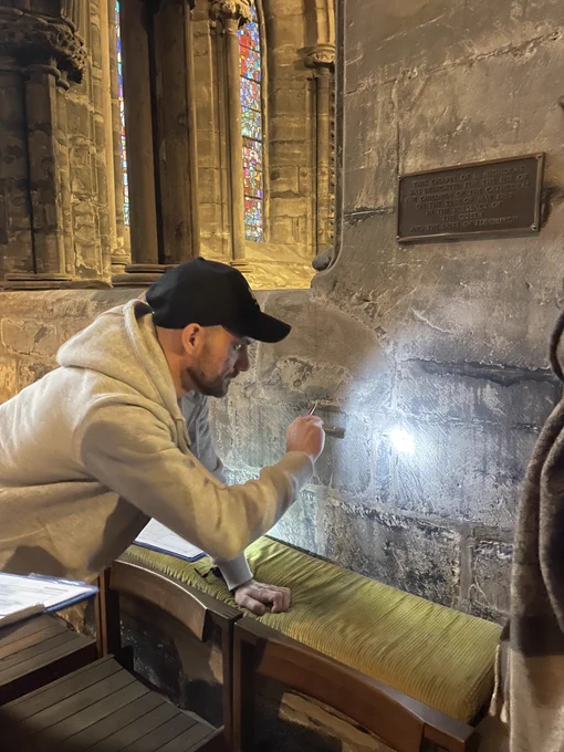 A person illuminating a mason's mark with a torch.