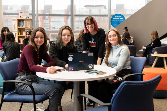 four students are gathered around a round table in the Dixon/Alger Fireside Reading Room at the North Oshawa Library. 
