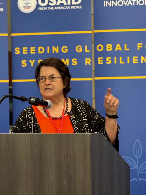 Person speaking at an event, standing at a podium with a microphone, against a backdrop with the USAID logo.