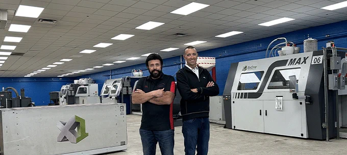 Two individuals standing with arms crossed in front of CNC machines in an industrial setting. The machines are labeled with the HAAS logo.