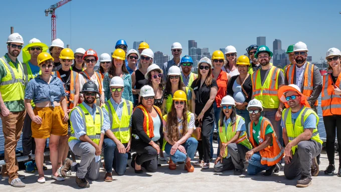 Group of people posing together on a solar installation site with Denver's skyline in the background.