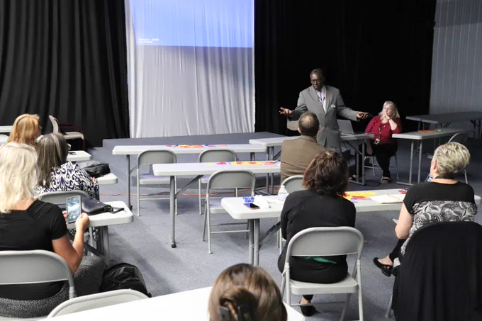 Photo of PLC attendees sitting at tables in an auditorium listening to a speaker at the front of the room.
