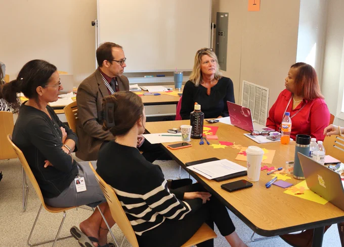 Photo of PLC attendees sitting at a table in a classroom having a discussion.