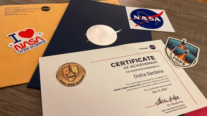 NASA TOPS swag including a physical copy of the certificate for completing NASA's Open Science 101 curriculum, a few stickers of NASA and NASA TOPS, and a folder with a NASA logo. 