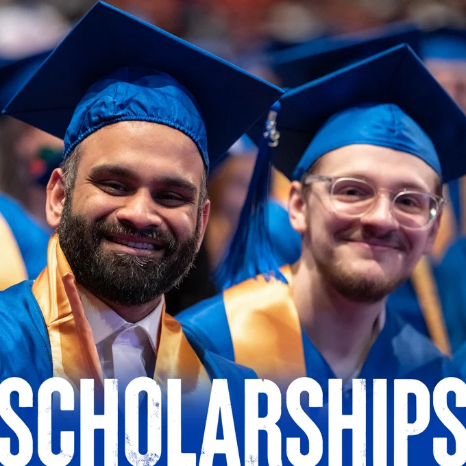 Two people wearing blue and gold commencement regalia smile at the camera