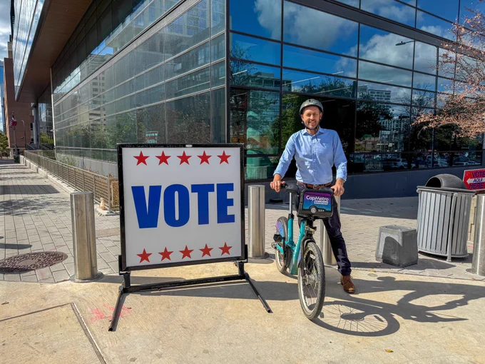 Photo of Travis County Judge Andy Brown in front of a sign that says “vote” at the Civil and Family Courts in downtown Austin.