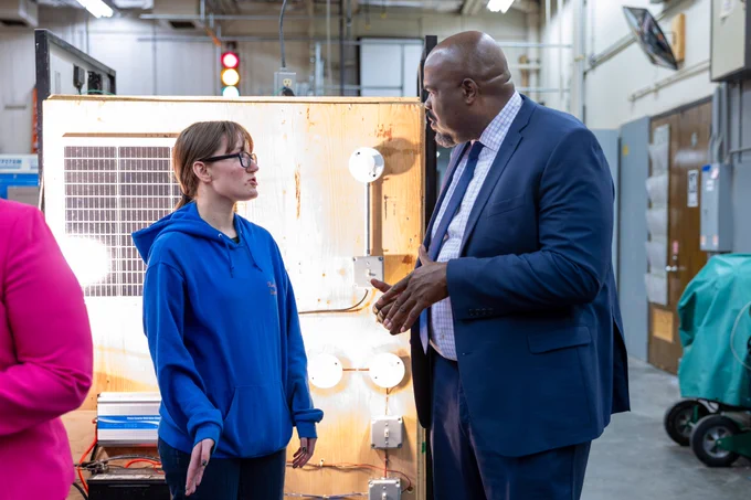 Education Secretary Tutwiler speaks to a student in front of an energy lab with lightbulbs in the background.