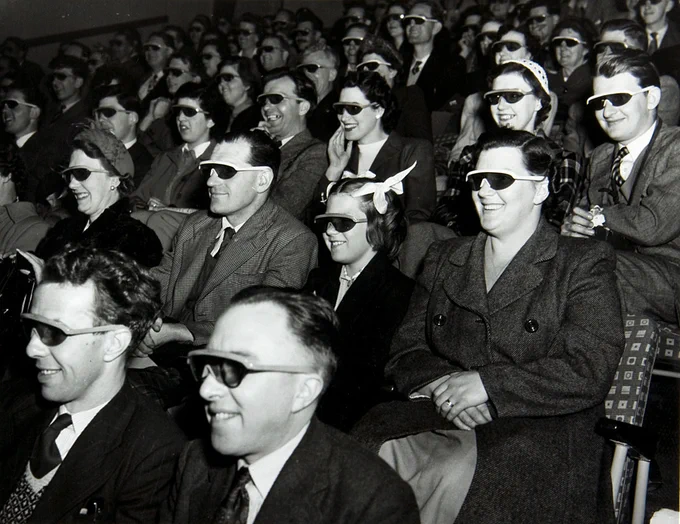 Black and white photograph of multiple rows of people sat in a theatre wearing 3D glasses and smiling, watching something out of shot. Festival of Britain, 1951. Catalogue reference: WORK 25/208 (3647)