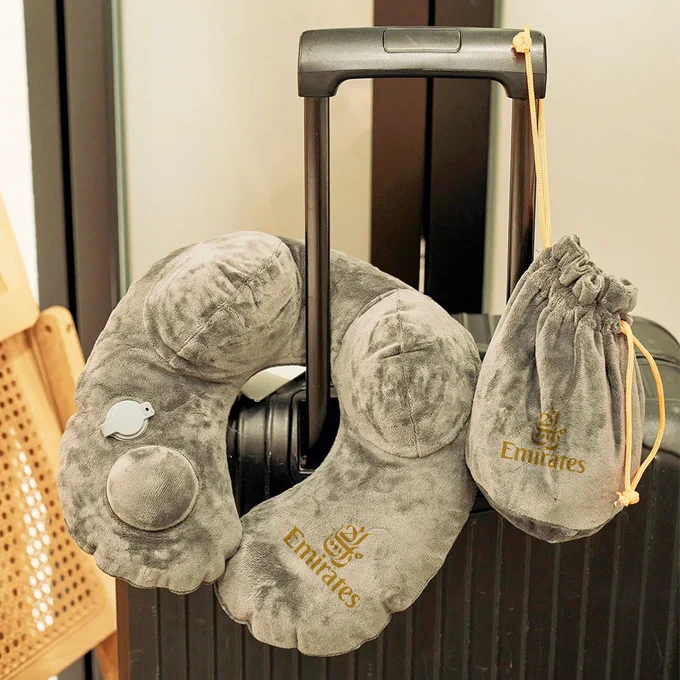 BrandHK’s auto-inflatable grey travel pillow resting on a suitcase handle, with a matching drawstring bag, showcasing its portability and plush design.