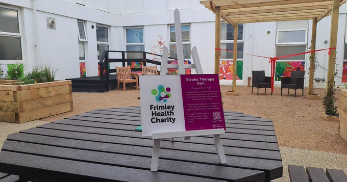 An outdoor rehabilitation area with a sign for the Stroke Therapy Unit sponsored by Frimley Health Charity. 