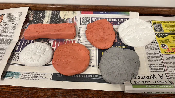 six small clay tablets of varying colours and shapes with 3-5 lines of Hittite cuneiform writing, arranged on newspaper