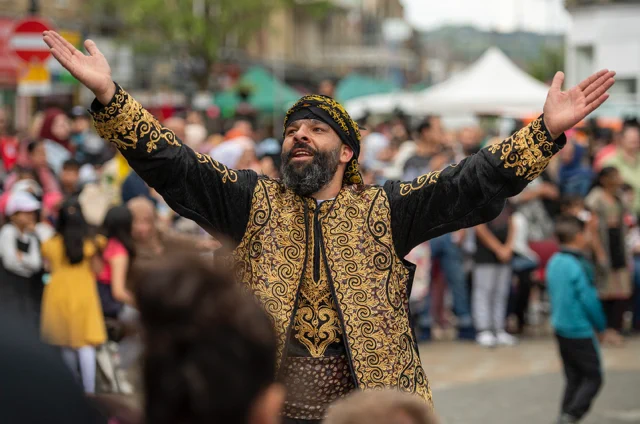 Colour photograph of a man in traditional south Asian costume with his hands in the air in celebration