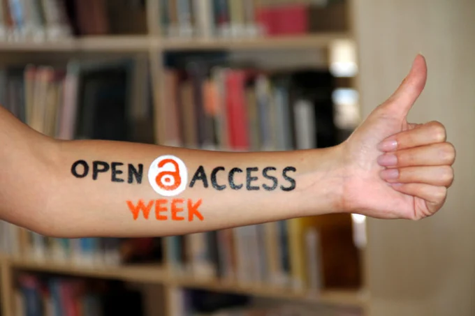 A forearm displays the phrase "OPEN ACCESS WEEK" painted in black and orange. The word "ACCESS" features an open access icon in orange within a white circle. The arm is positioned in front of a blurred bookshelf background and is making a thumbs-up gesture. "WEEK" is painted in orange, while "OPEN ACCESS" is in uppercase black letters.

Photo Credit (CC BY 4.0): Tatyana Zaytseva (http://legacy.openaccessweek.org/photo/great-oaw-at-khazar-library-2)
