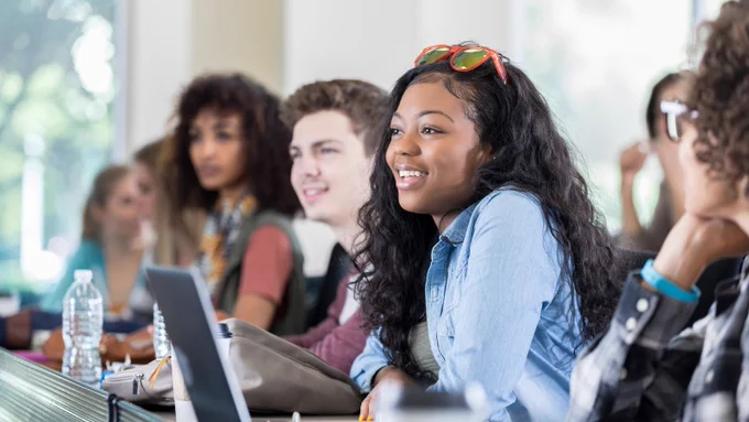 College students sitting together in a row of a classroom, engaged in discussion.