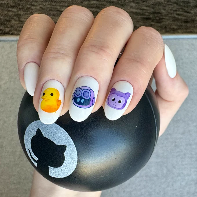 Hand holding a black GitHub ball with GitHub logo, nails are painted white and the 3 middle nails have artwork on them: Mona our mascot, Copilot, and a duck.