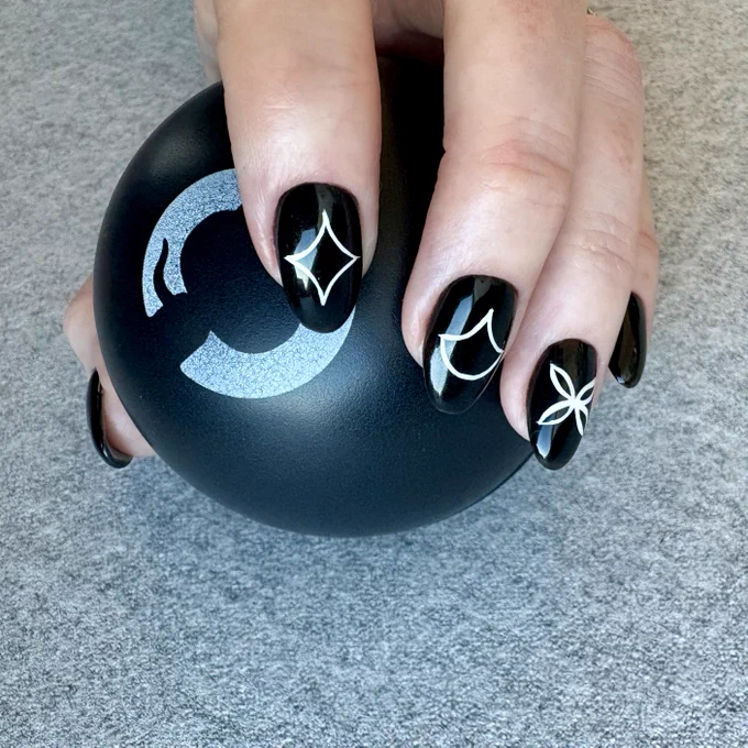Hand holding a black GitHub ball with GitHub logo, nails are painted black with the middle 3 fingers decorated with white graphic shapes matching the  GitHub Universe patterns.