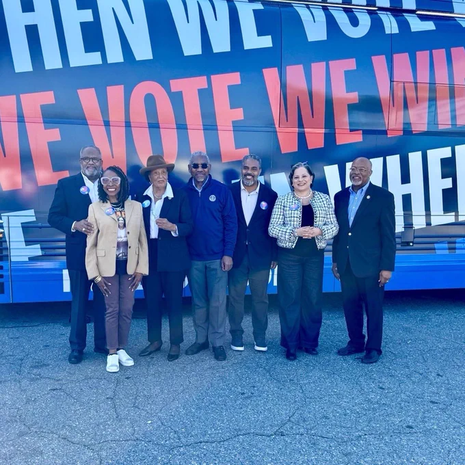 Photo of Reps. Troy Carter, Yvette Clarke, Alma Adams, Greg Meeks, Steven Horsford, Glenn Ivey, and me standing in front of a large bus. Text reads “When we vote, we win!”