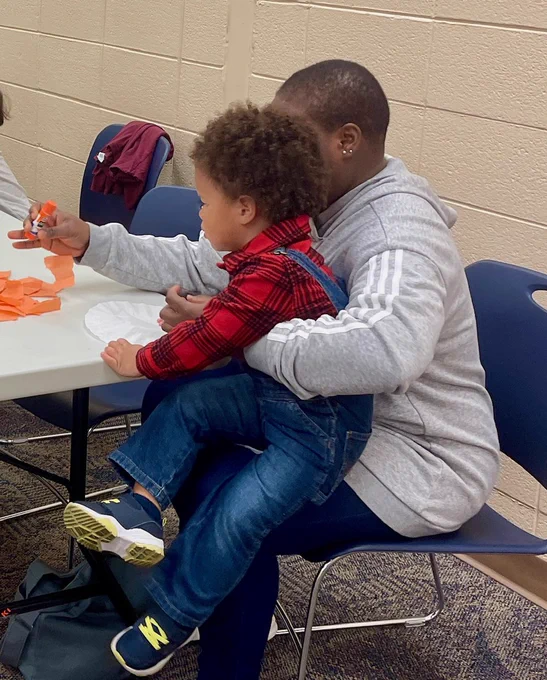 A child in someone's lap as they work on the tissue paper pumpkin together